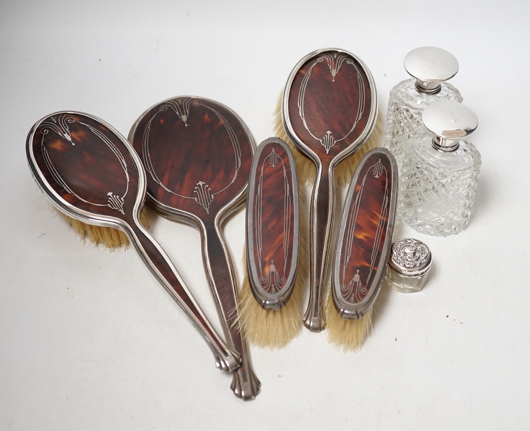 A George V silver and tortoiseshell pique mounted dressing table set, Adie Bros, Birmingham, 1934, and three silver topped toilet jars.